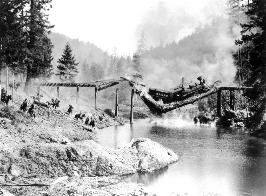 Black and white still of a bridge and train collapsing over a river