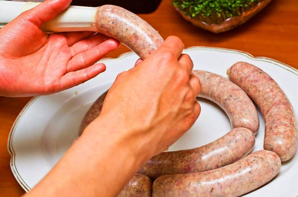 Hands making sausage cases above a plate of sausages