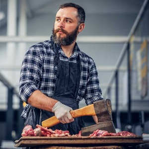 Young bearded man in an apron chopping meat