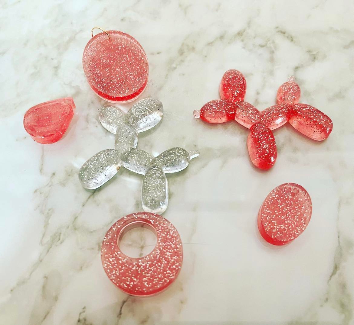 pink and transparent glittery resin balloon dogs and ovals on marble surface